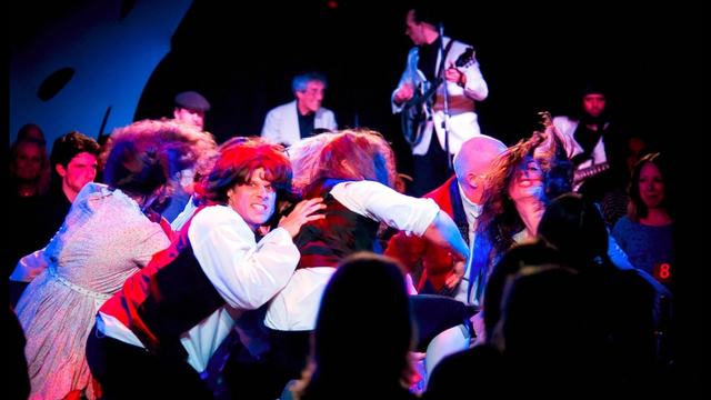 The Frow Show cast mid-sketch on stage, with the live band playing behind them