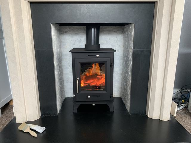 A lit wood-burning stove in a tiled fireplace opening